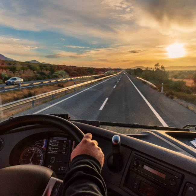 View from the driver’s seat of a truck of the ... View from the driver's seat of a truck of the highway and a landscape of fields at dawn.